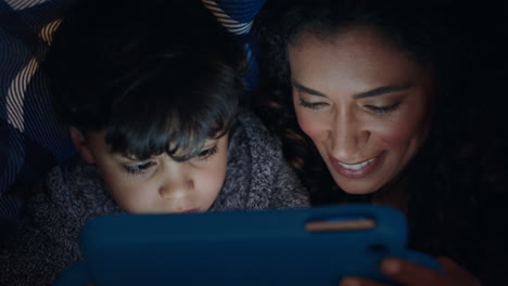 Glückliche-Mutter-Und-Sohn,-Die-Unter-Der-Decke-Einen-Tablet-Computer-Benutzen.-Kleiner-Junge-Spielt-Spiele-Auf-Touchscreen-Technologie,-Während-Sich-Die-Mutter-Vor-Dem-Schlafengehen-Entspannt-Und-Spaß-Hat