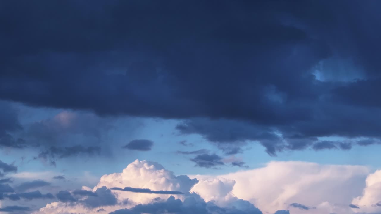 Drone hyperlapse showing dramatic storm clouds over Spain, with white cumulonimbus below and dark cumulus above against a deep blue summer sky. A striking natural time-lapse of weather formation