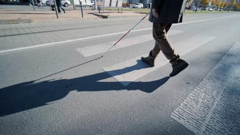 hombre con discapacidad visual cruzando la carretera con su palo con la ayuda de la acera táctil para peatones para discapacitados visuales en la ciudad.