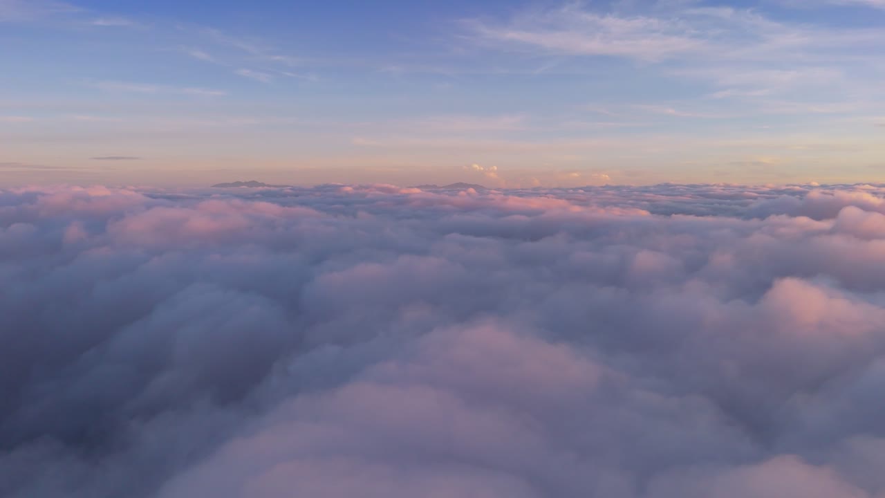 Stunning aerial view above a sea of fluffy pink and orange clouds at sunrise. A dreamy cotton candy cloudscape with deep blue sky offering ample copy space for text