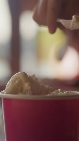 un niño pequeño recoge helado de vainilla con una cuchara desechable de una taza de papel sentado en un café en primer plano. un niño disfruta de un helado para almorzar en la cantina