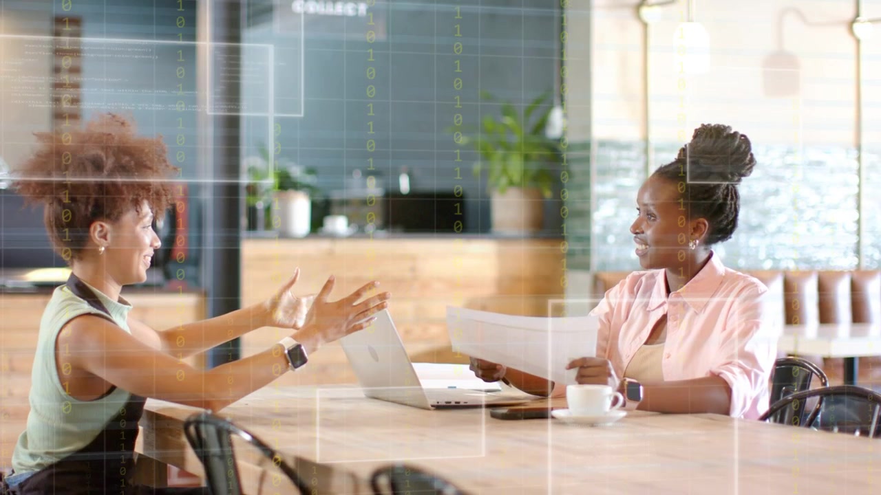 Right woman showing pages, left woman leaning and gesturing while both reviewing business on laptop