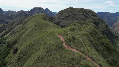 aerial follows narrow grass ridge trail in rugged mountain landscape