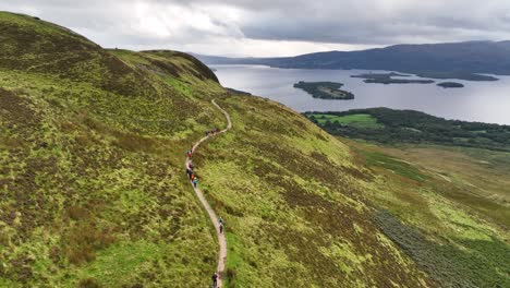 cinematic aerial sweep of hillwalkers climbing conic hill