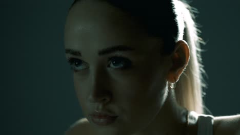 closeup shot of a woman’s face during indoor cycling, with a smooth camera move from side profile to front, revealing her intense focus and determination in cinematic studio lighting conditions