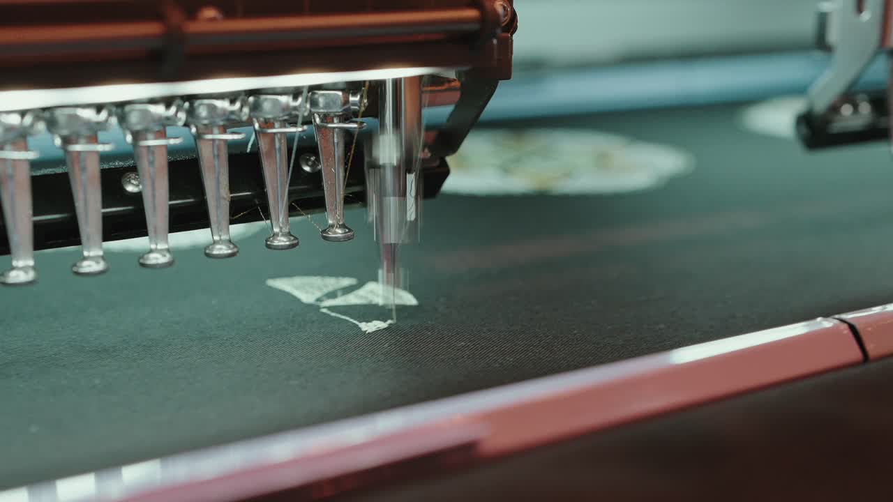 industrial embroidery machine stitching a white design on dark fabric in precise motion
