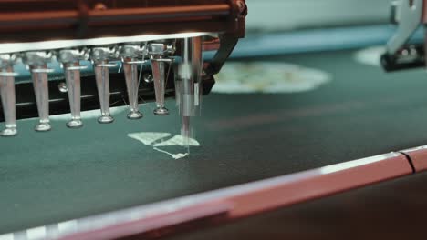 industrial embroidery machine stitching a white design on dark fabric in precise motion