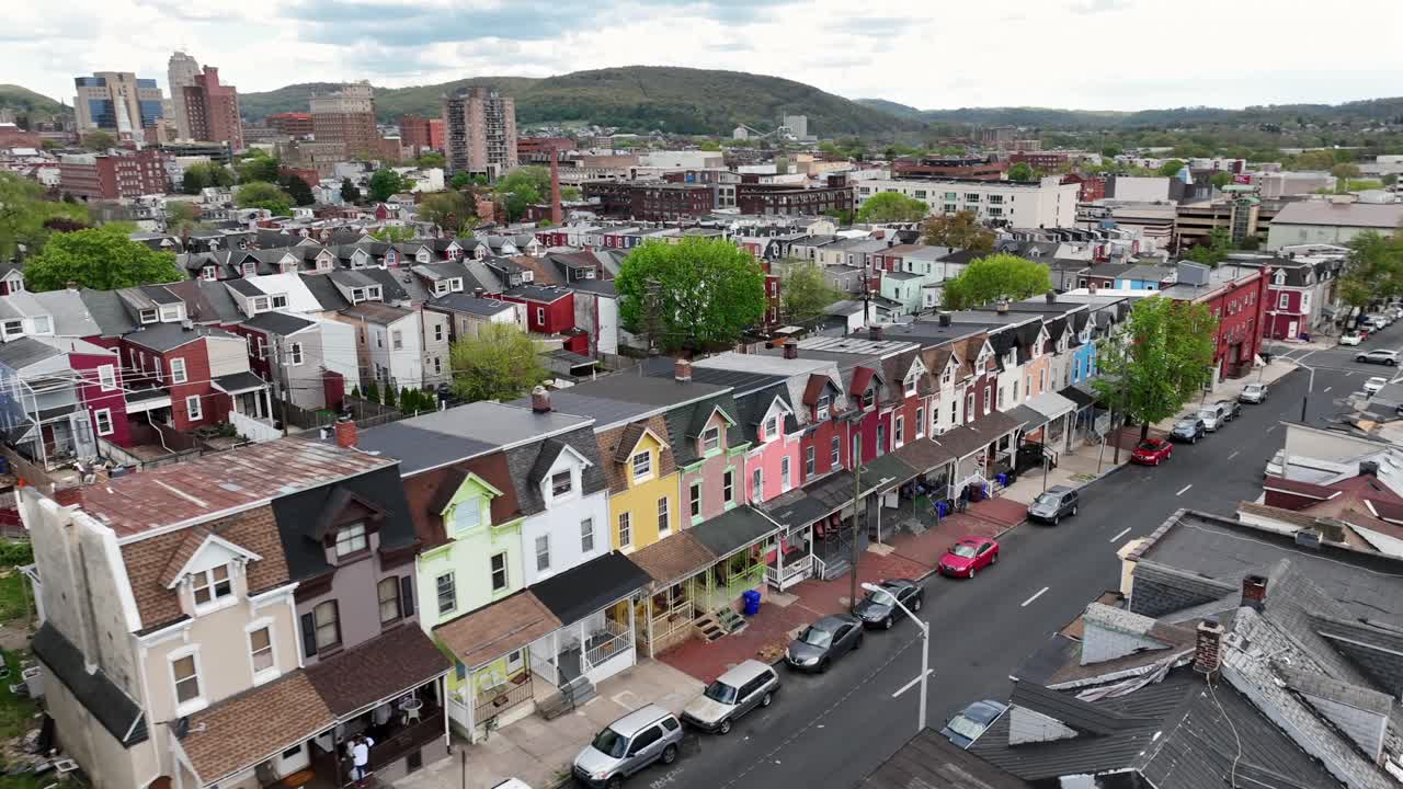 Aerial view of a vibrant residential neighborhood with colorful row houses lining a street and a city skyline in the background