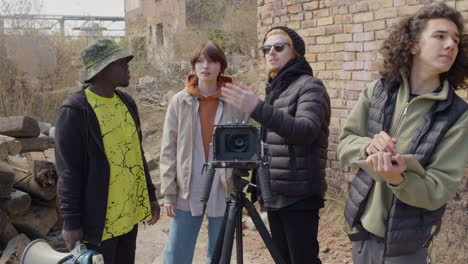 three production coworkers talking about a recording project in front of a camera on a tripod in the street while another worker taking notes 1