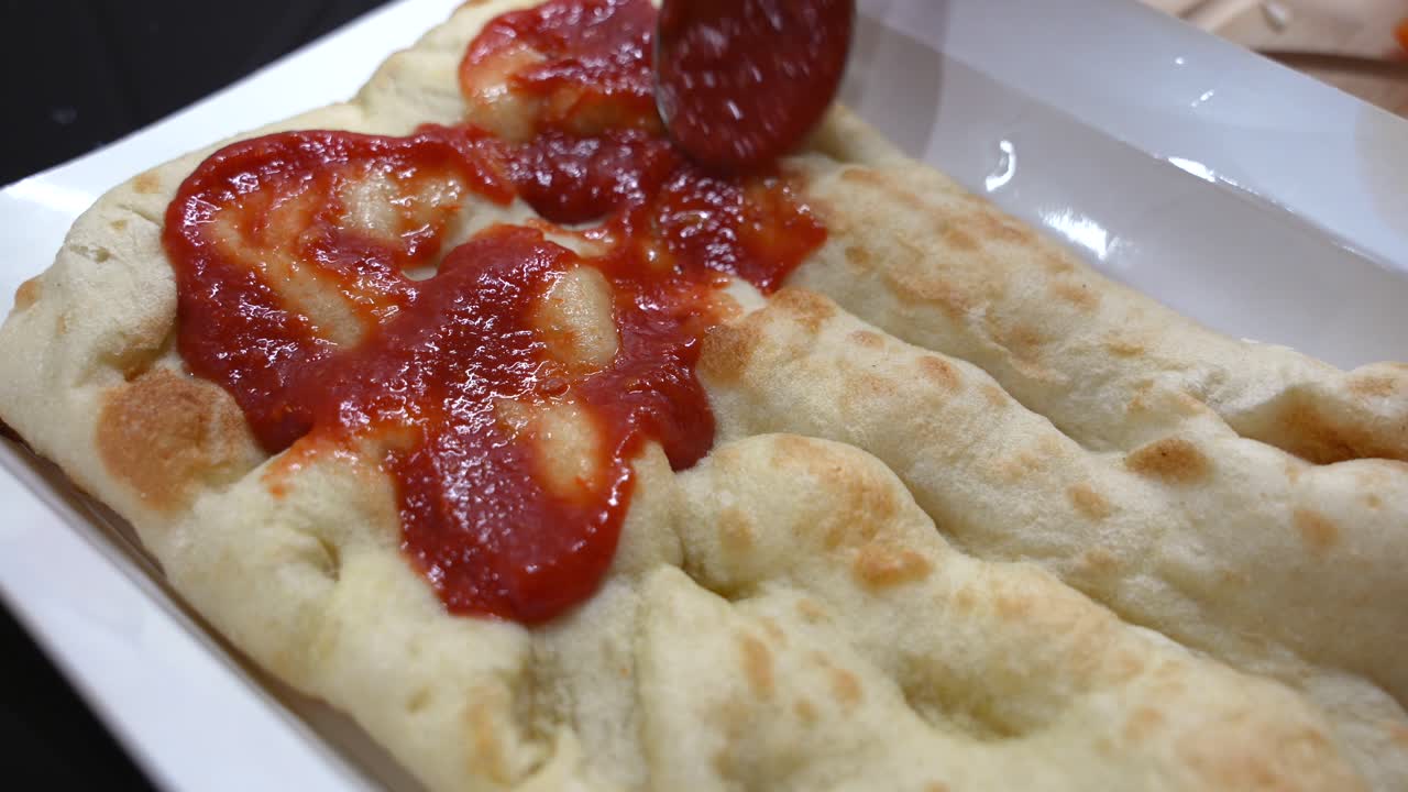 Spreading tomato sauce on pizza base. Making homemade dinner with pinsa dough