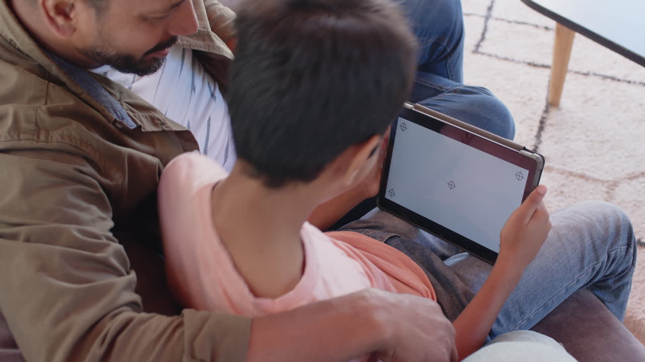 Indian father and young son using tablet together while sitting on couch, copy space