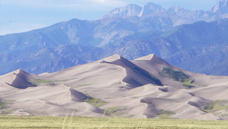 Stunning-late-summer-opening-view-of-The-Great-Sand-Dunes-National-Park-Colorado-Rockies-mountain-sandy-14er-peaks-crisp-golden-yellow-tall-grass-wind-clouds-blue-sky-mid-day-cinematic-down-pull