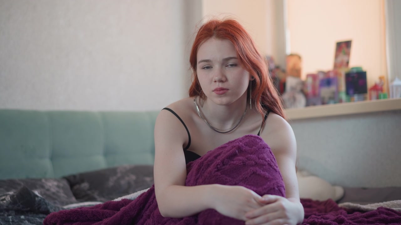 Yatak odasında, yatakta mor battaniyeye sarılmış Kafkas kızıl saçlı falcı. Pencereden süzülen yumuşak sabah ışığı, düşünceli bir ifade, pencere pervazında tarot desteleri ve kristallerle samimi, sinematik bir atmosfer.