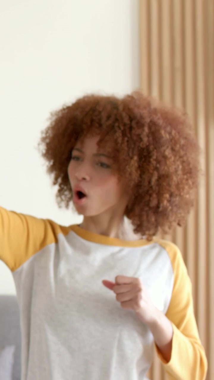 Vertical video: Hearing friend talking, woman in raglan top pointing, clapping near sofa, slat wall