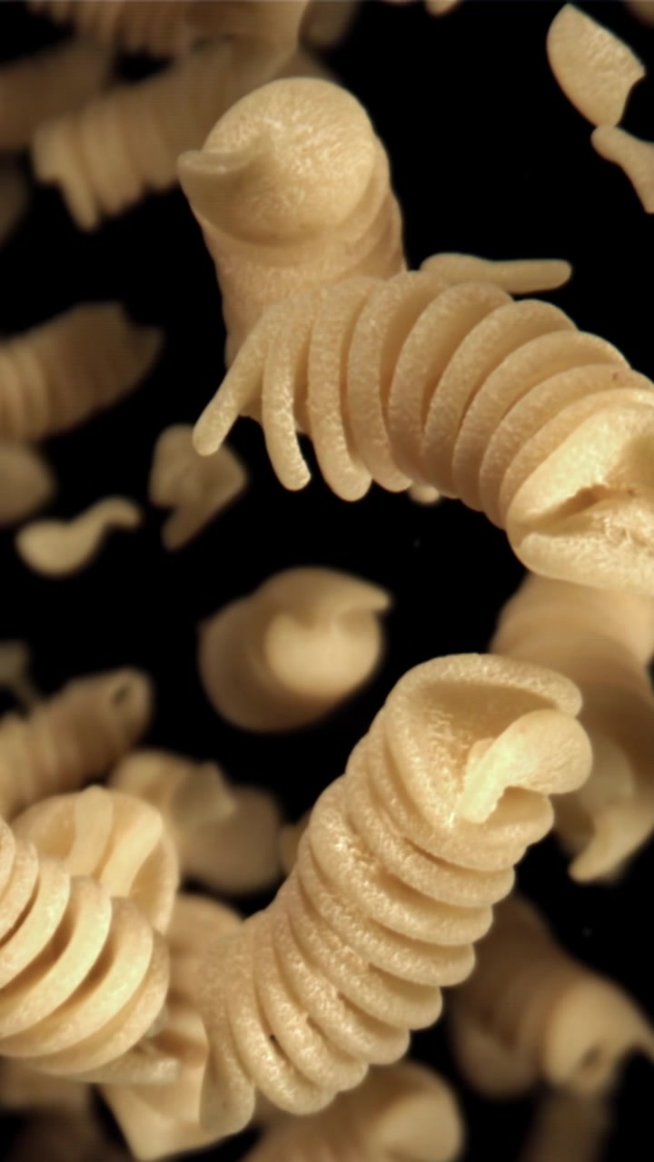 Close-up Pasta Fusilli Kering Jatuh dalam Gerakan Lambat dengan Latar Belakang Hitam
