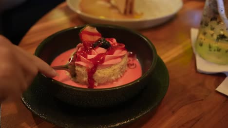 female hand cut a piece of strawberry pink cake dessert with a spoon