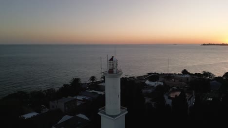 aerial view orbiting colonia del sacramento old city lighthouse with glowing sunrise on the uruguay horizon