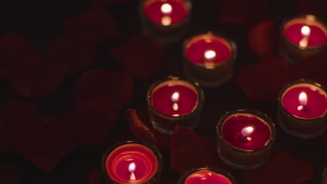 romantic lit red candles on background covered in rose petals