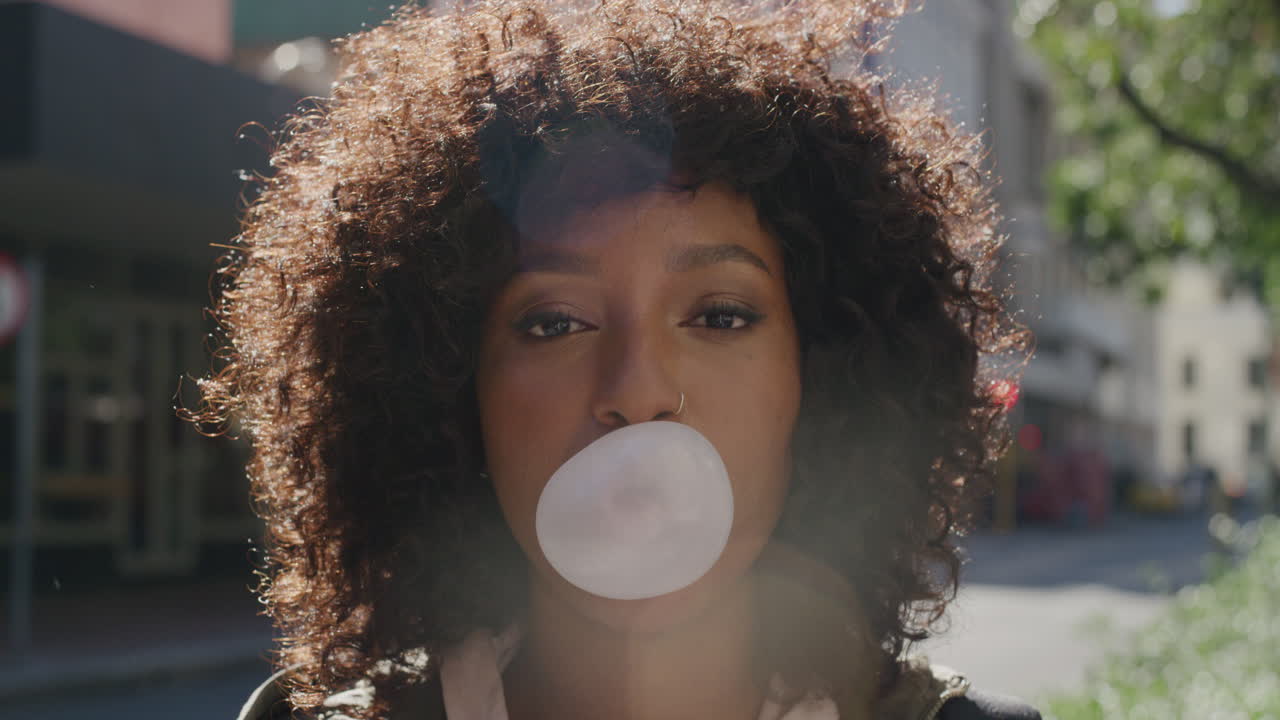 close up portrait of young african american woman blowing bubblegum smiling happy enjoying playful fun in sunny urban city street morning female student with afro hairstyle