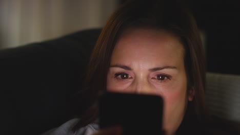 un primer plano de una mujer ansiosa sentada en el sofá en casa por la noche mirando su teléfono móvil preocupada por las redes sociales o las malas noticias