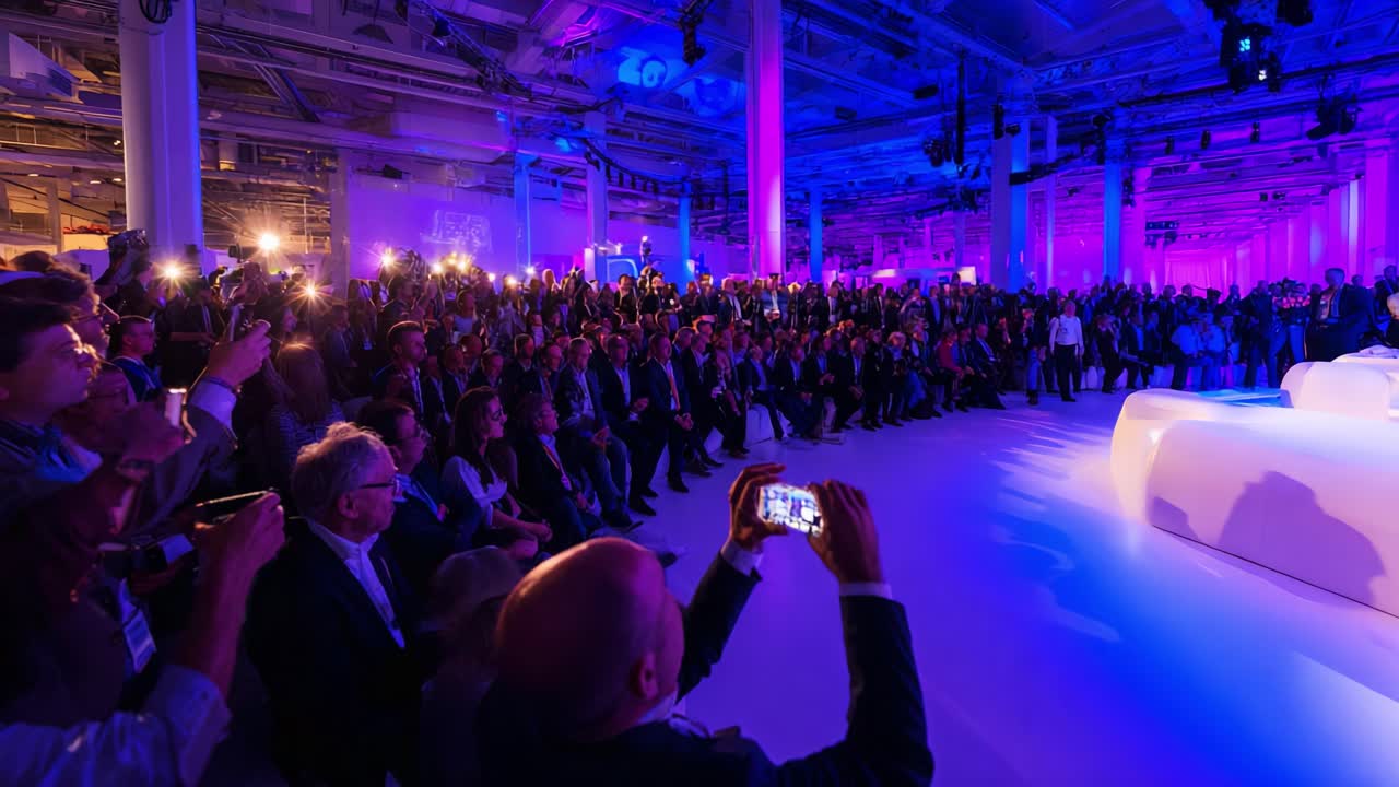 A lively and vibrant audience captivates the atmosphere of a prominent event, illuminated by colorful lights and capturing moments on their devices, creating a dynamic visual spectacle