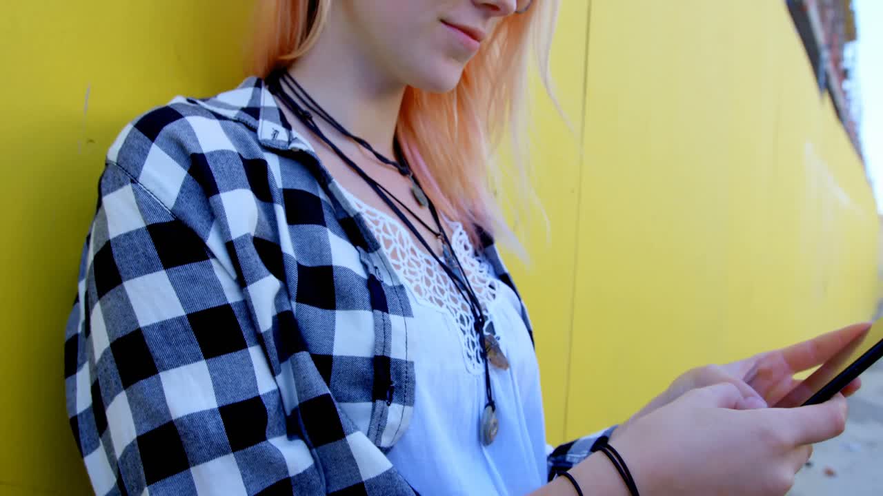 модная женщина использует мобильный телефон против желтой стены в переулке 4k