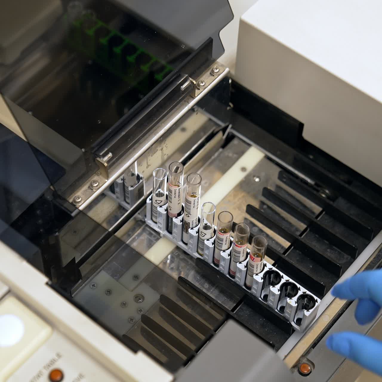 Gloved hand of a laboratory expert puts the stand with test tubes into equipment. Machine for blood test analysis in modern hospital