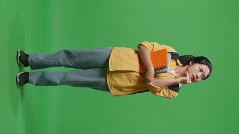 full body of asian woman student with a backpack and some books thinking and looking around while standing in the green screen background studio