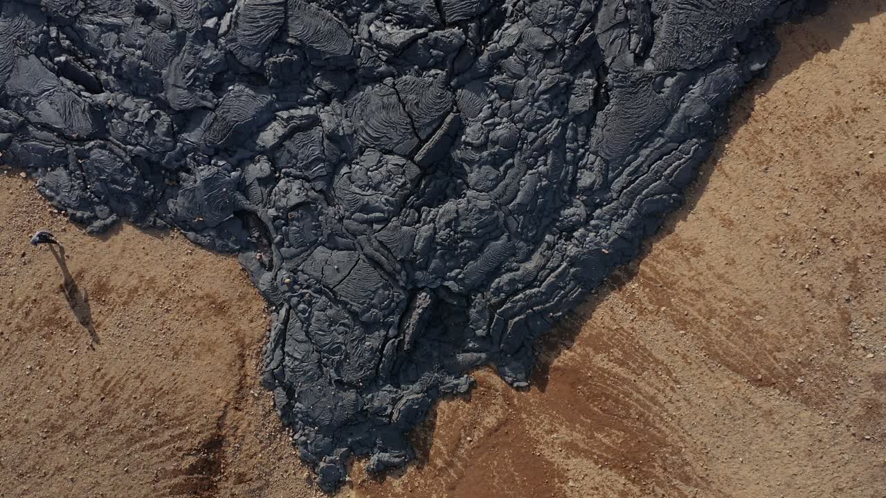 Edge of black basalt lava field with cracked surface rock, Iceland