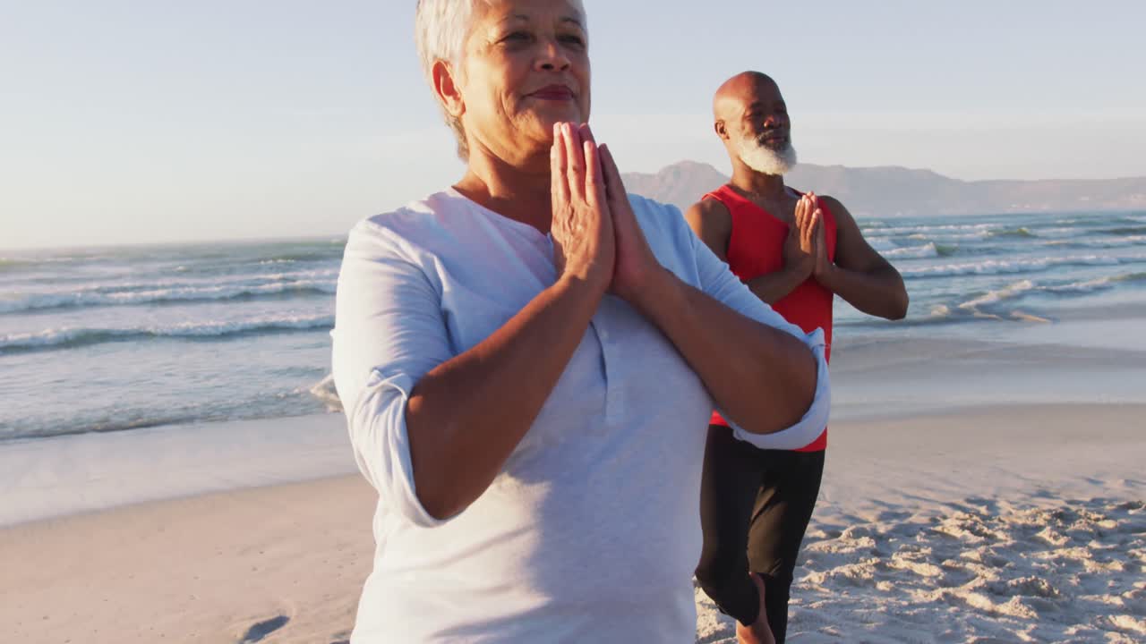 Coppia anziana afroamericana che pratica yoga in spiaggia