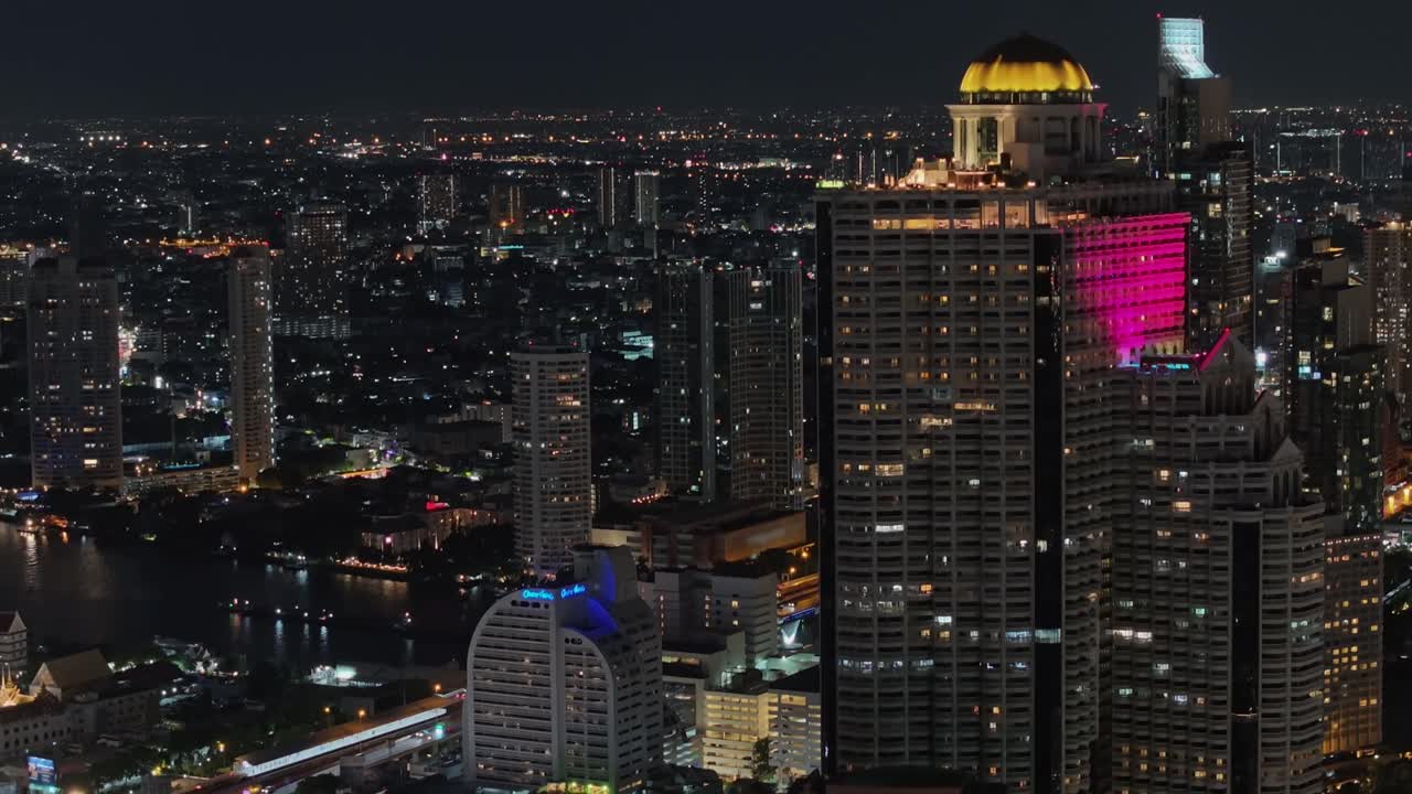 Cinematic drone shot of Bangkok at night showing glowing skyscrapers, city lights, and river reflections. Stunning aerial view of Thailand's capital