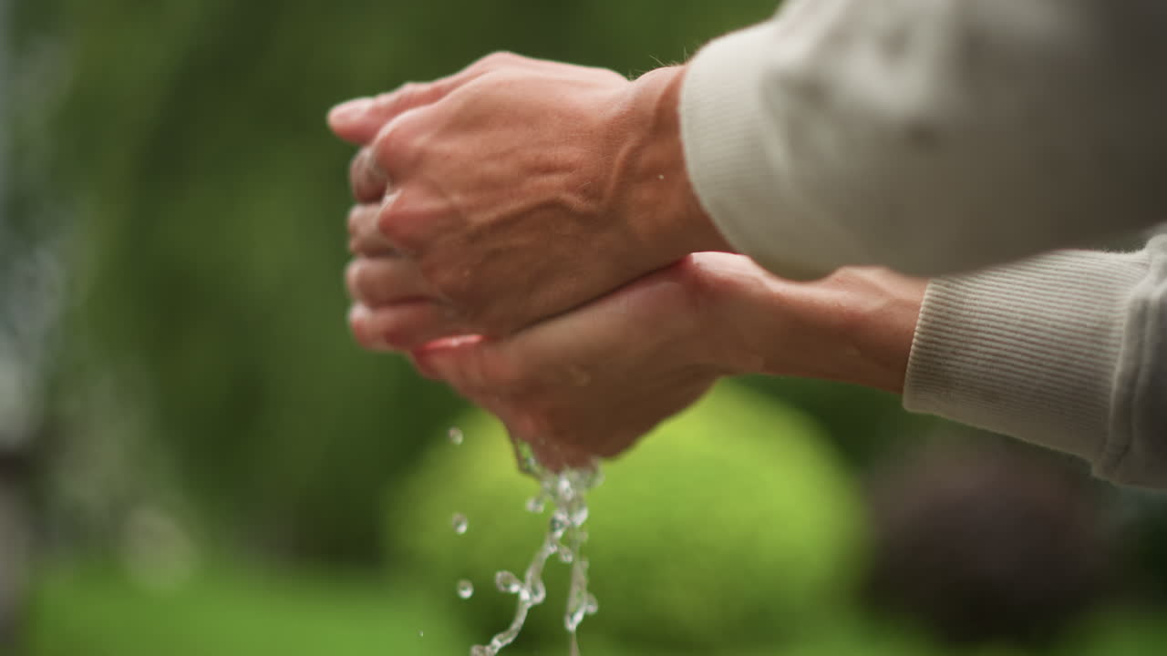 백인 손이 웅덩이 표면을 스치듯 지나가고, 손가락 끝으로 반사되는 파티오와 윤기 있는 젖은 포장 도로, 초록색 덤불 그림자에 잔물결을 만들고, 장난기 넘치는 조경 디자이너가 물에 흠뻑 젖은 재료를 시험하고 있어요.