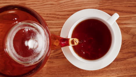 pouring tea from a glass teapot into a white cup