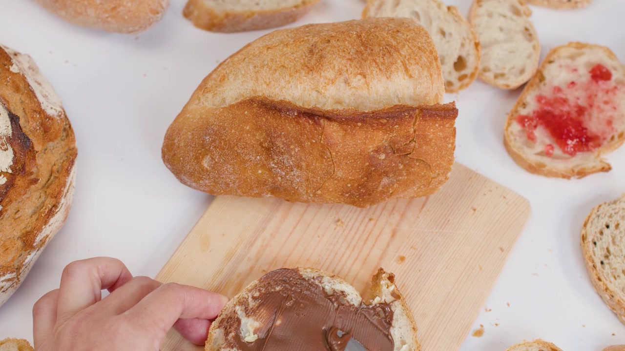 Close-up overhead shot of hand spreading chocolate hazelnut cream on bread over white background.