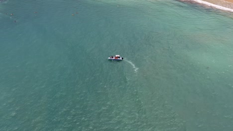 Drone-Aéreo-Ojo-De-Pájaro-Inclinado-Hacia-Abajo-Después-De-Un-Pequeño-Barco-De-Delfines-Navegando-En-Aguas-Tropicales-Turquesas-Del-Océano-Con-Turistas-Cerca-De-La-Playa-De-Madeiro-En-Pipa,-Brasil-Rio-Grande-Do-Norte-En-Un-Día-De-Verano