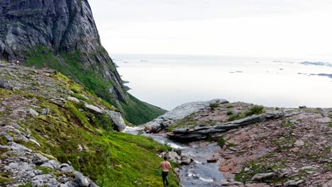 hombre sin camisa corriendo al borde del río que fluye a través de una cascada con vista al océano en noruega