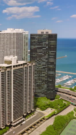 huge high rise buildings and skyscrapers towering over busy traffic roads and yacht club. eye-catching scenery of chicago architecture at backdrop of blue horizon. vertical video