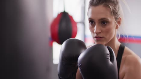 video of confident, determined caucasian woman in boxing gloves training with punchbag at a gym