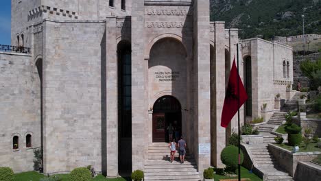 skanderbeg museum stone facade with albanian flag, tourists entering in arched gates