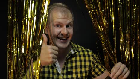 Portrait-of-caucasian-man-posing-on-black-background.-Gold-shining-foil-strips.-Party,-music,-disco