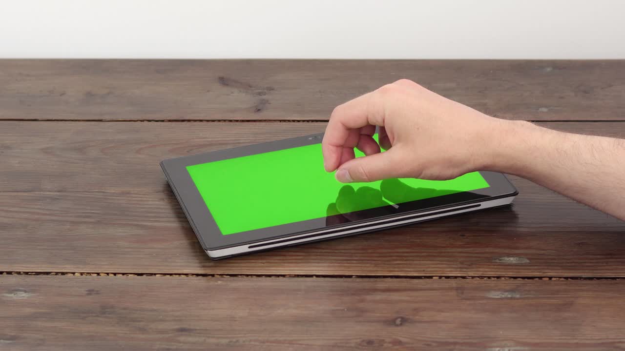 una tableta con una pantalla verde en una mesa de madera, hace un zoom con un dedo.