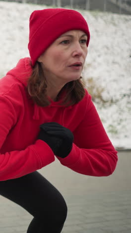 entrenador con capucha roja demuestra ejercicio de lanzamiento lateral durante el entrenamiento de invierno al aire libre en un terreno pavimentado cubierto de nieve rodeado de colina nevada con barandilla de hierro, en clima frío