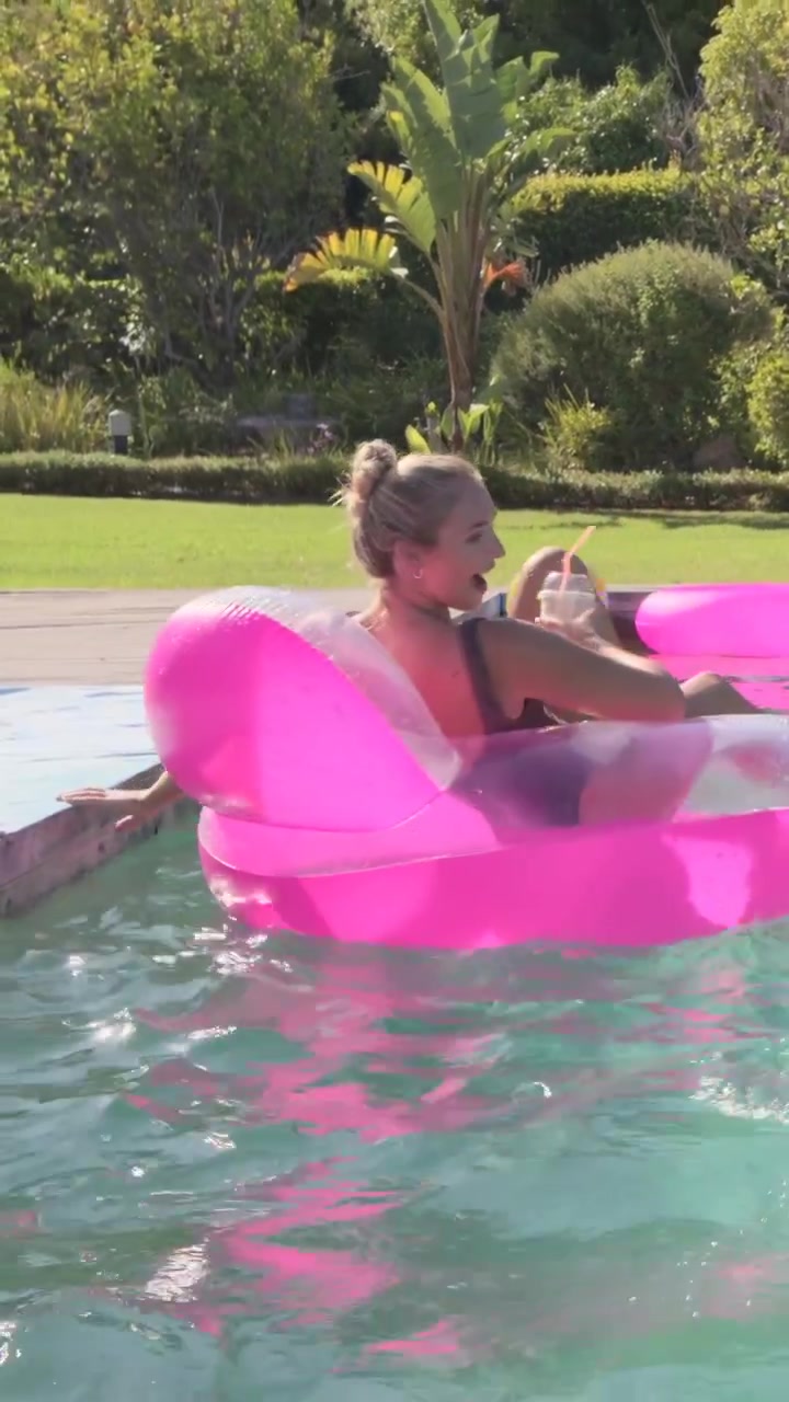 Vertical video: Woman in black suit reacting to big splash, paddling pink float at pool, steadying