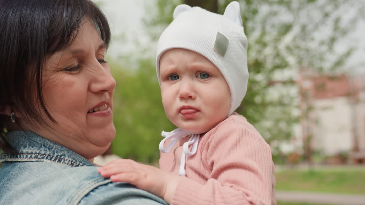 Elderly Woman With Child Outdoors, Grandmother Holding Her Grandchild Amid Blooming Trees In Park, Caucasian Grandmother In Pink Attire Gently Embraces Her Baby Amidst Spring Blossoms In Park