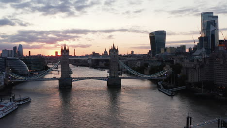 Fly-above-River-Thames.-Slide-and-pan-shot-of-old-Tower-Bridge-against-colourful-sunset-sky.-London,-UK