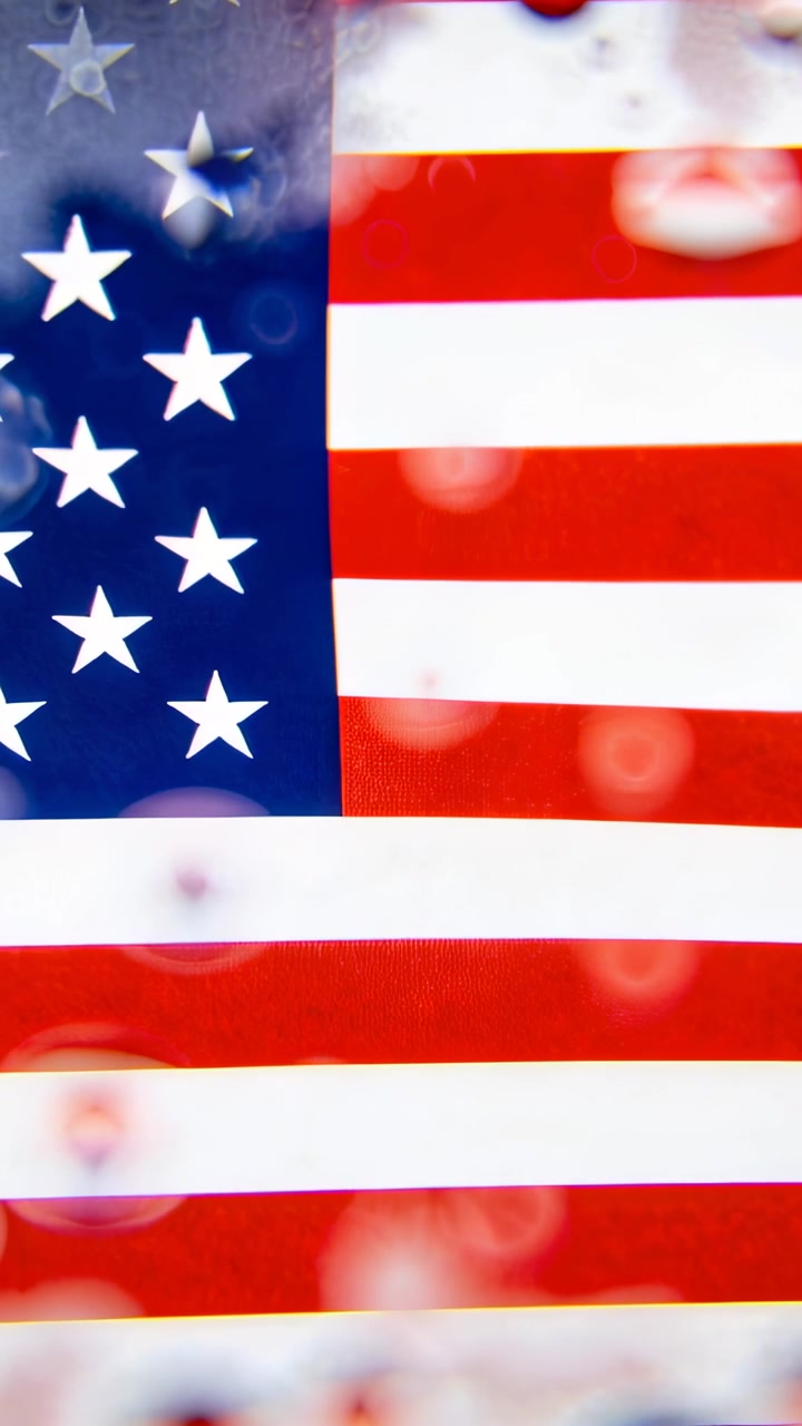 Video verticale: Telecamera in movimento che alterna la messa a fuoco su una bandiera americana con goccioline e bokeh sul vetro.