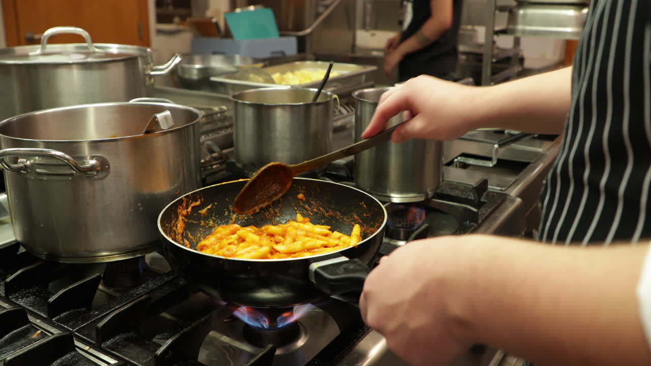 chef experto revolviendo pasta penne con salsa roja en una sartén en la cocina de un restaurante