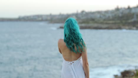 saliendo, una joven descalza de cabello azul con un vestido blanco que fluye gira y camina hacia el océano, copia el espacio