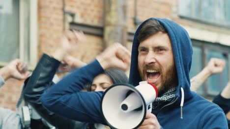 close-up view of caucasian man in hoodie yelling on a loudspeaker in a protest with multiethnic group of people in the street