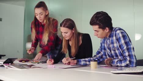 Group-of-young-hipster-people-working-together-in-modern-office.-Young-professionals-making-sketches-sitting-at-the-table,-preparing-their-new-project-and-drinking-coffee-in-slowmotion